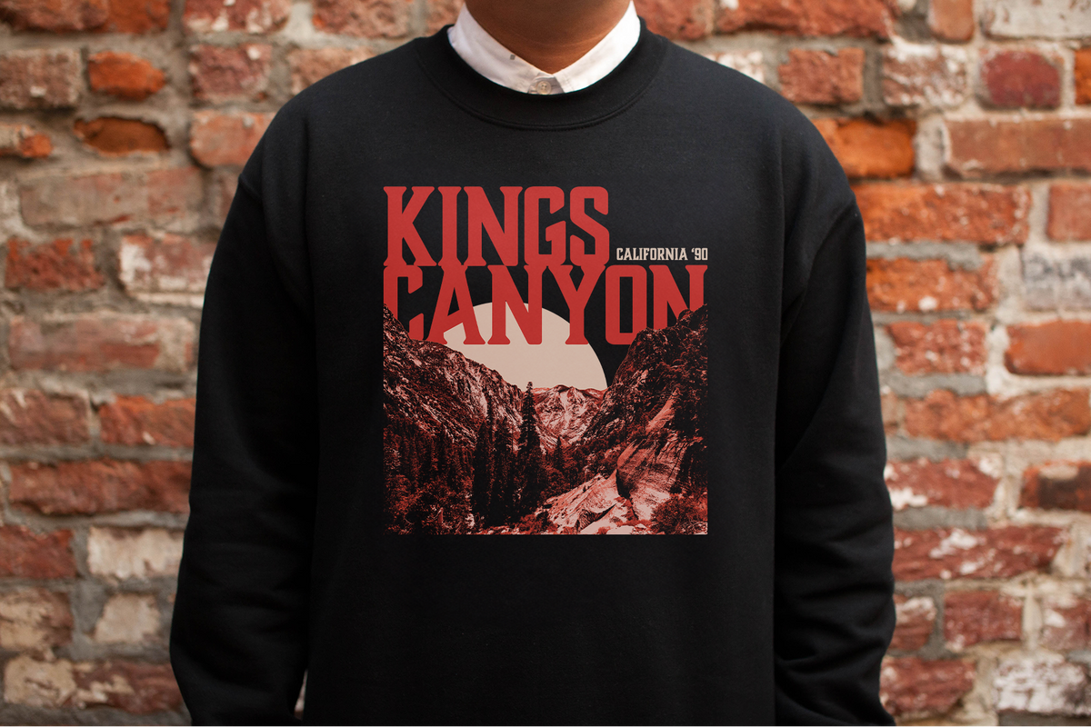 Person wearing a black sweatshirt with 'Kings Canyon' graphic against a brick wall.