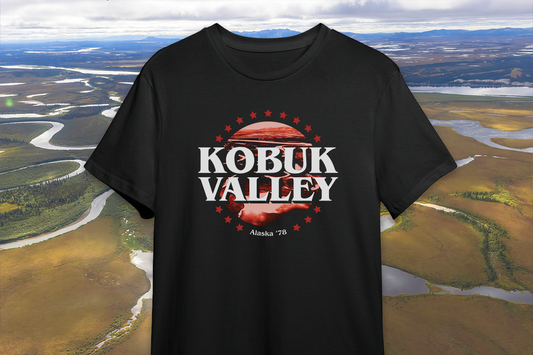 A black t-shirt with a red and white 'Kobuk Valley' design, in front of a scenic background