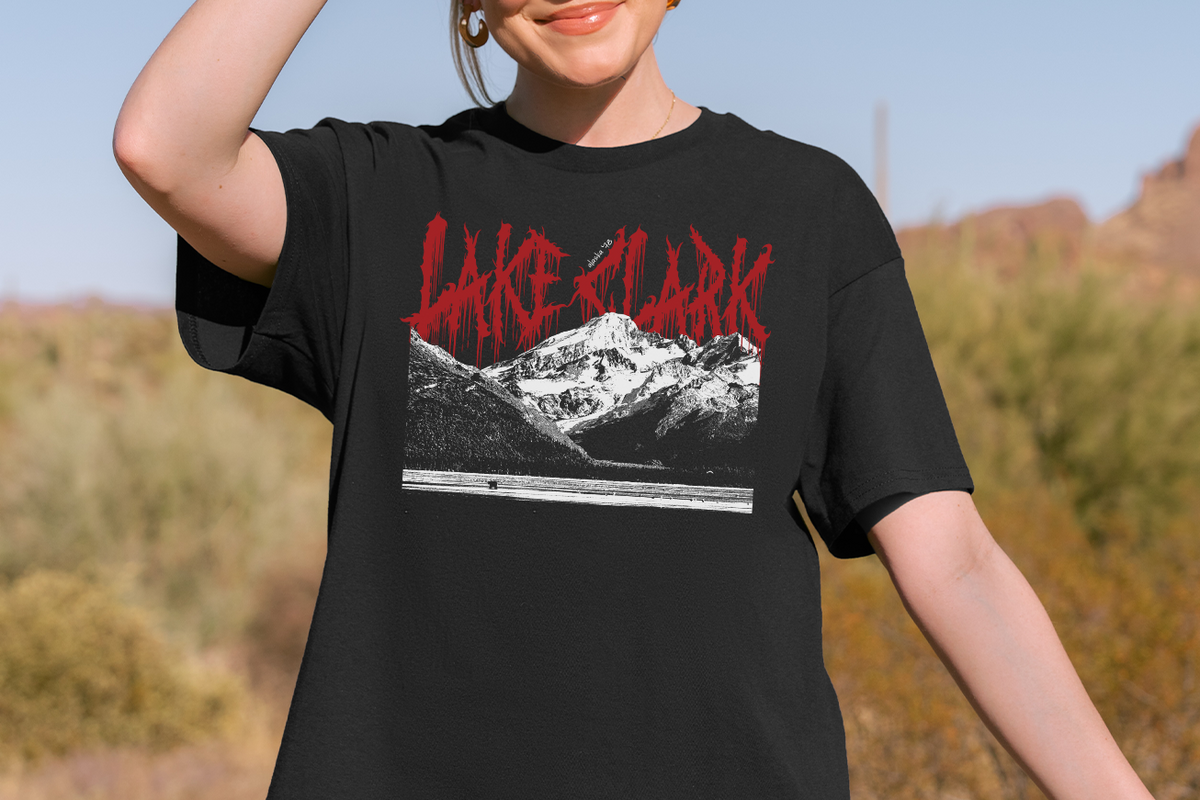 Person wearing a black t-shirt with a 'Lake Clark' graphic design of mountains and red text outdoors.