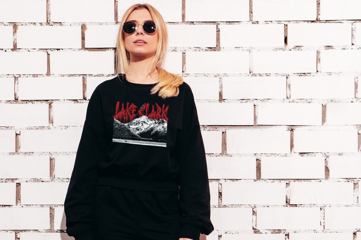 Person wearing a black sweatshirt with red text and graphic design against a white brick wall.