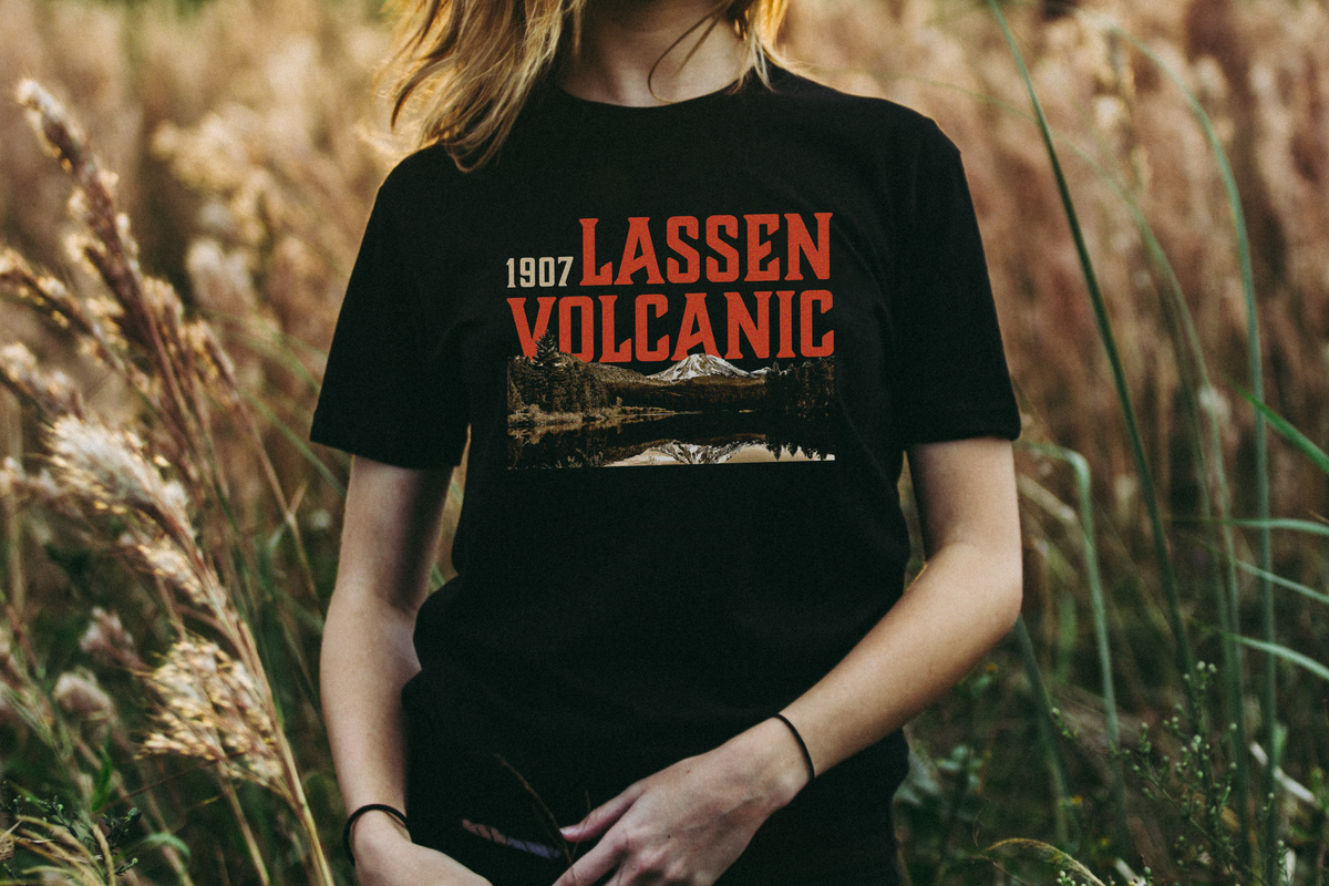 Person wearing a black t-shirt with 'Lassen Volcanic' design in a field.