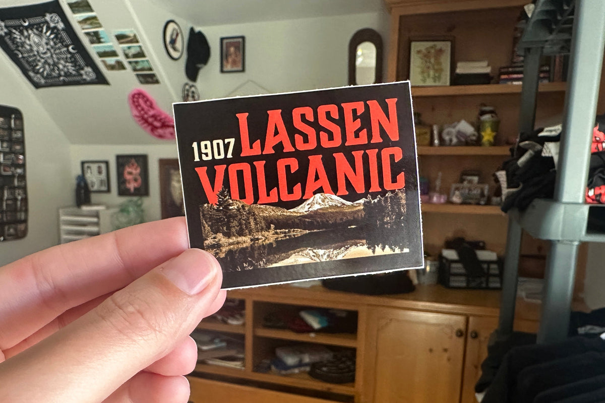 Hand holding a vintage-style Lassen Volcanic National Park sticker with a scenic image.