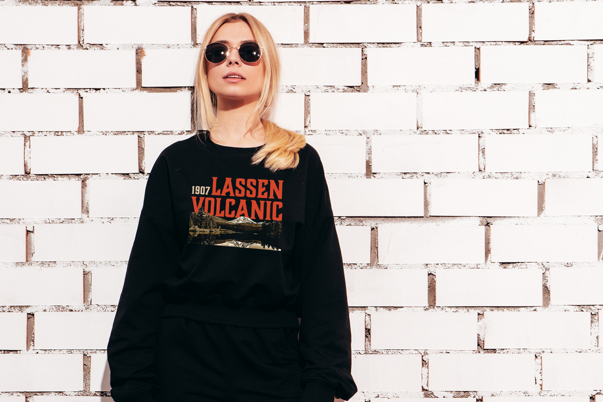 Person wearing a black sweatshirt with 'Lassen Volcanic' text against a white brick wall.