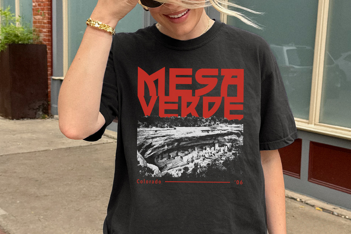 Person wearing a black t-shirt with 'Mesa Verde' graphic design outdoors.