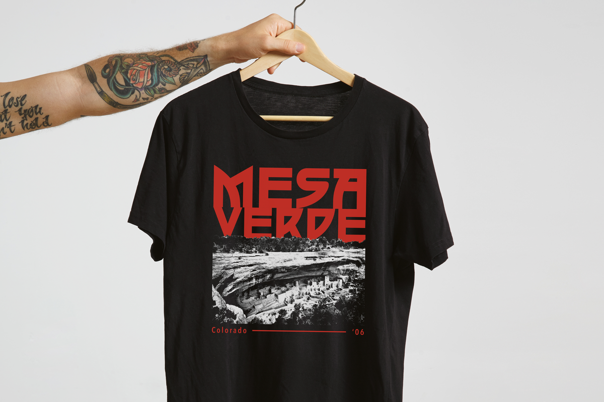 Black t-shirt with red and white 'Mesa verde' graphic design on a hanger against a light gray background