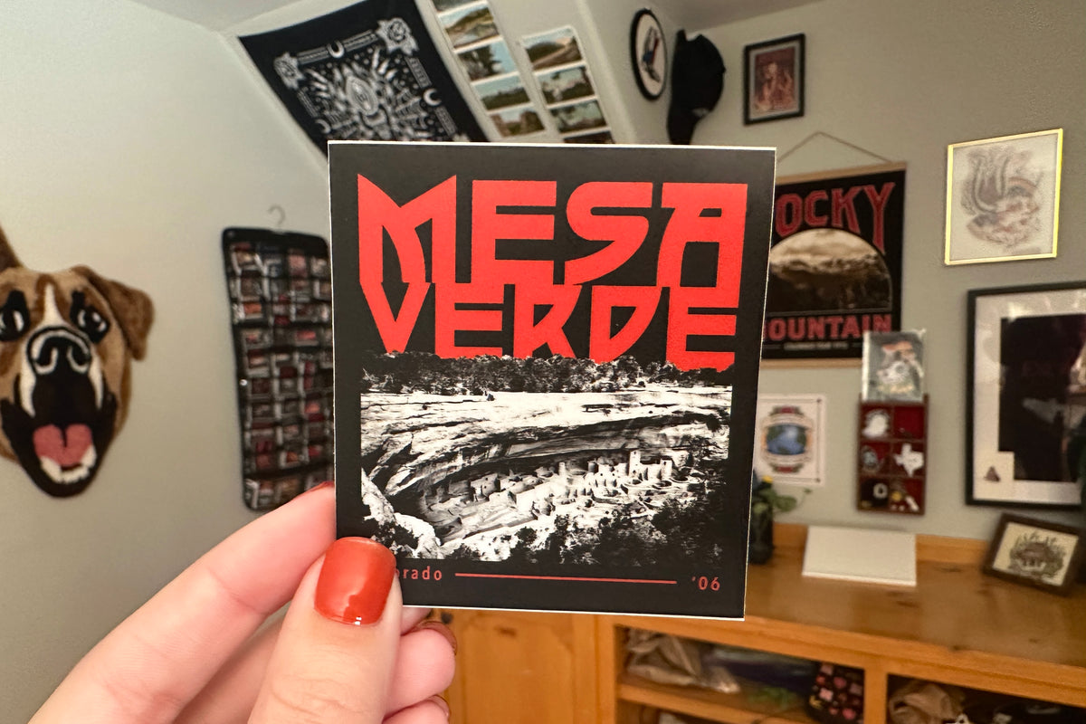 Person holding a 'Mesa Verde' sticker with a room in the background.
