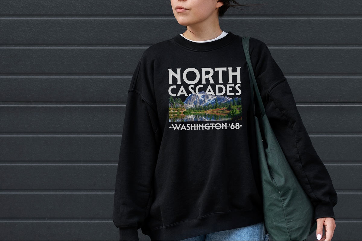 Person wearing a black sweatshirt with 'North Cascades' design against a gray wall.