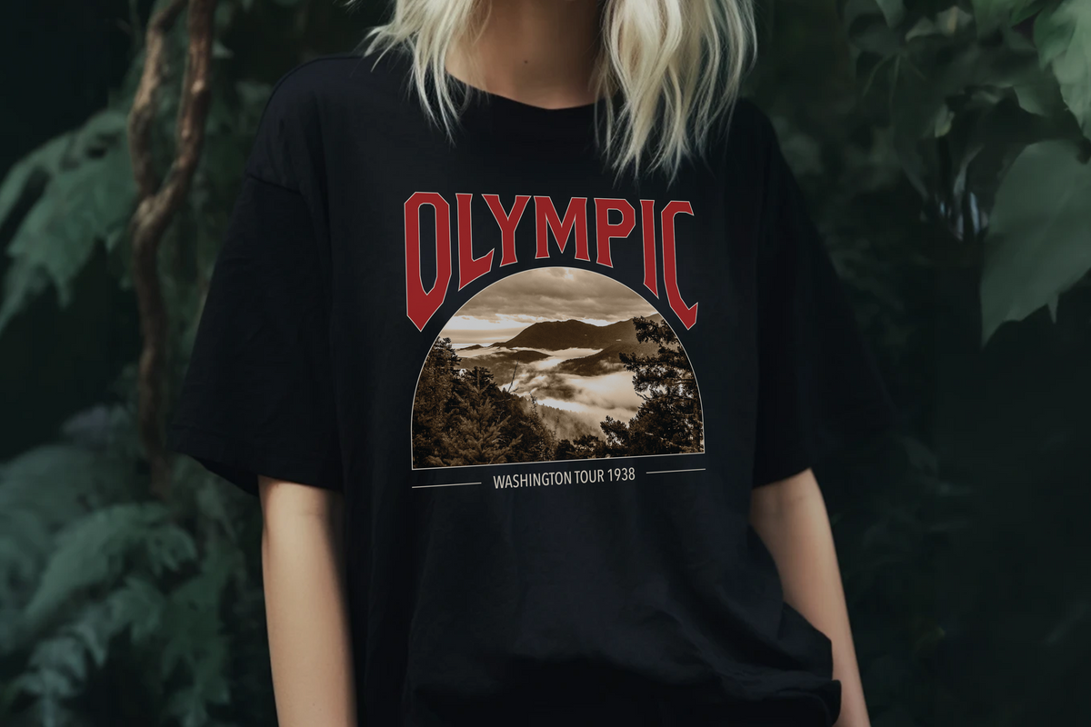 Person wearing a black t-shirt with 'Olympic' graphic design in front of green foliage