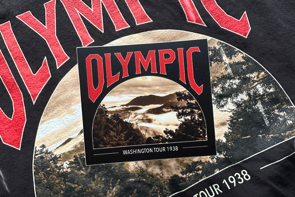 Black sticker with a red and white 'Olympic' design, in front of a textured background