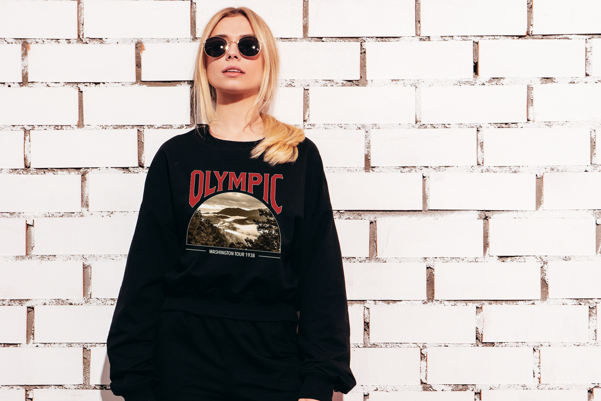 Person wearing a black sweatshirt with 'Olympic' design against a white brick wall