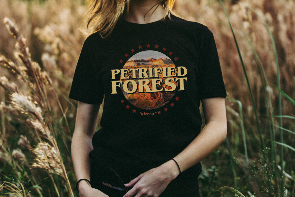 Person wearing a black t-shirt with 'Petrified Forest' design in a field