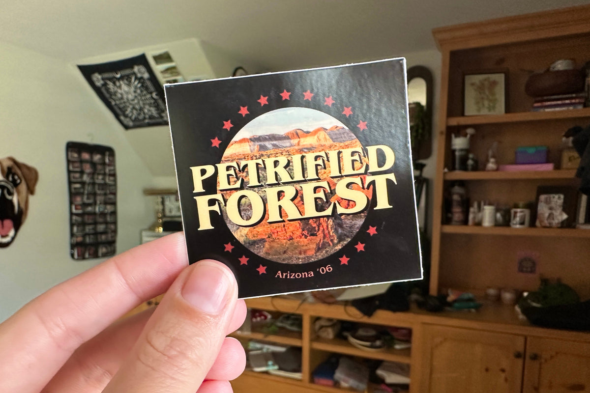 Sticker with 'Petrified Forest' text held in front of a wooden cabinet.