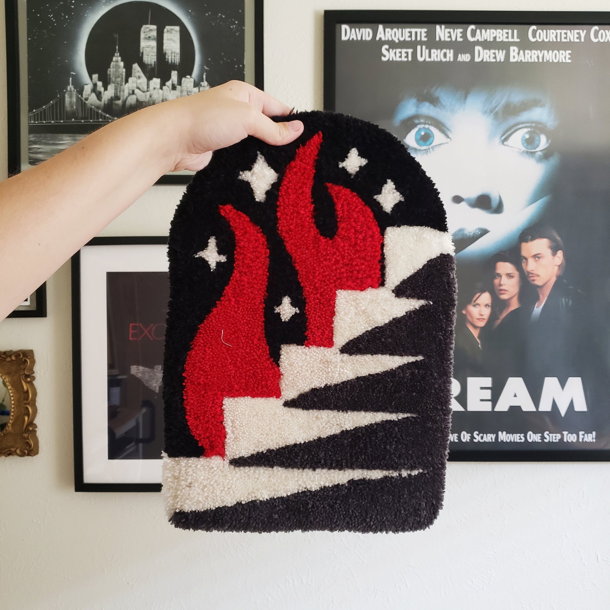 A tufted wall hanging depicting fire, stars, and stairs, against a wall