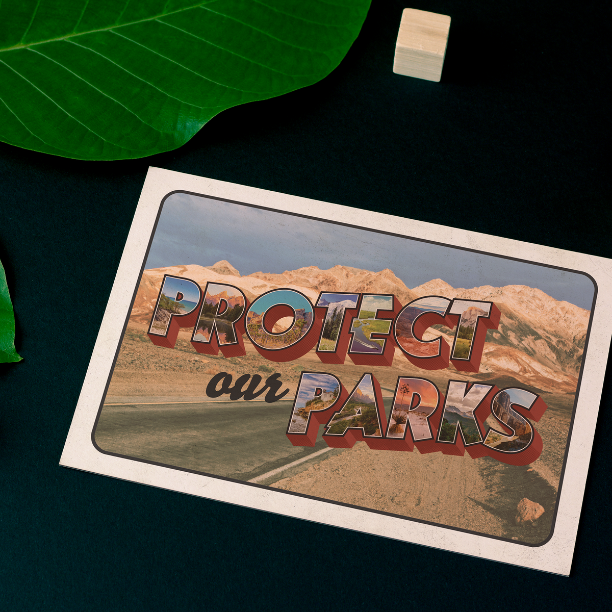 A postcard laying on a table, with the image of a desert road and the words 'Protect Our Parks'
