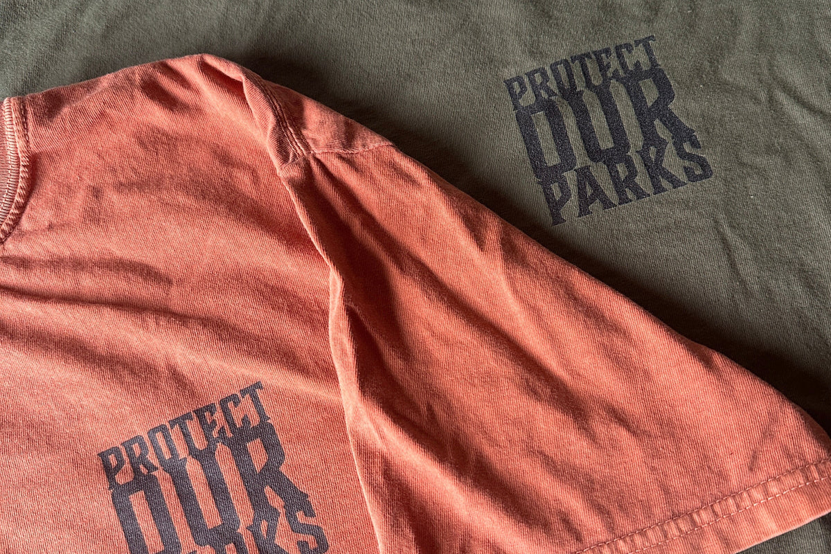 Two pairs of shirts, one orange and one green, with 'Protect Our Parks' text on a dark background.