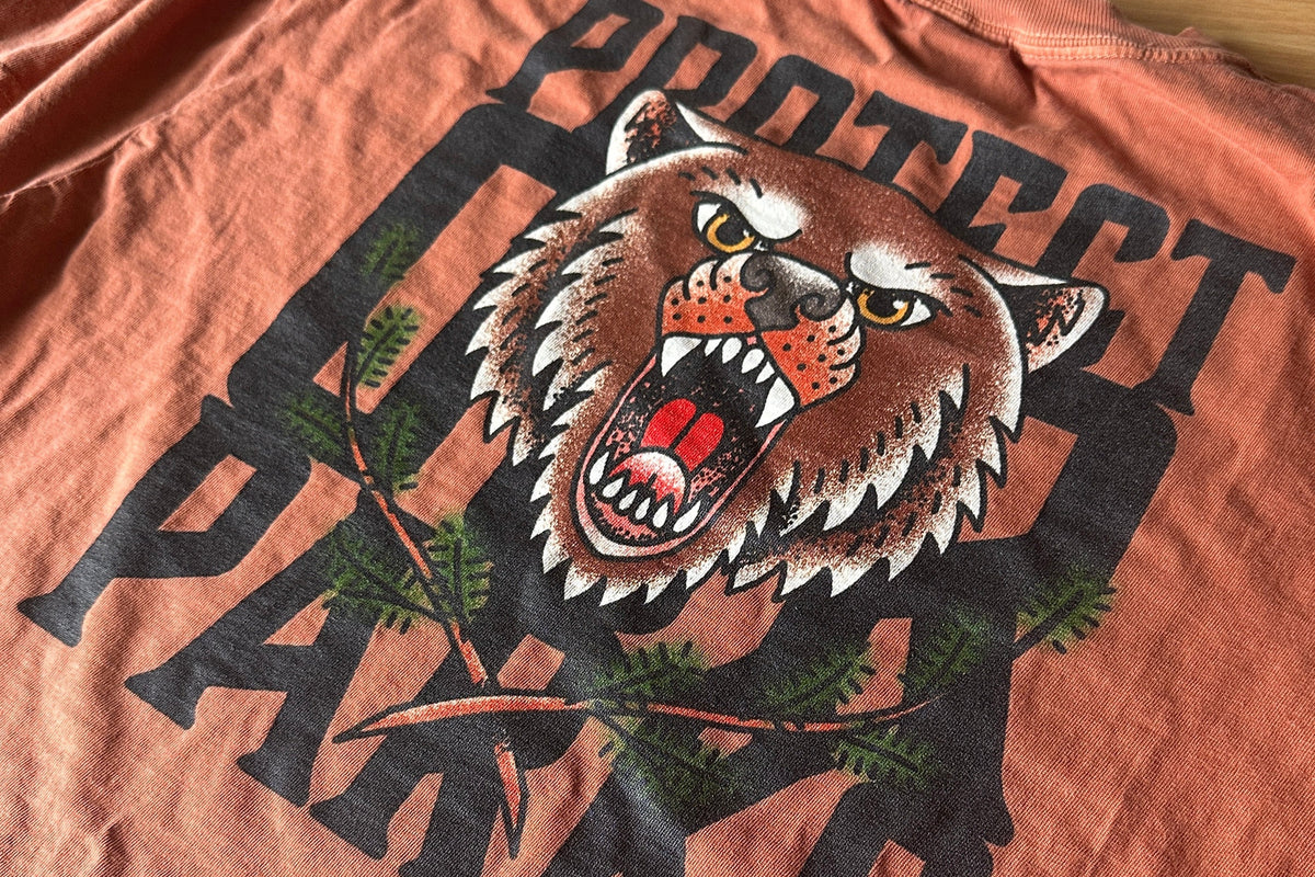 T-shirt with a graphic of a roaring bear and the text 'Protect Our Parks' on an orange background.