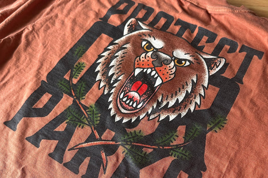 T-shirt with a graphic of a roaring bear and the text 'Protect Our Parks' on an orange background.