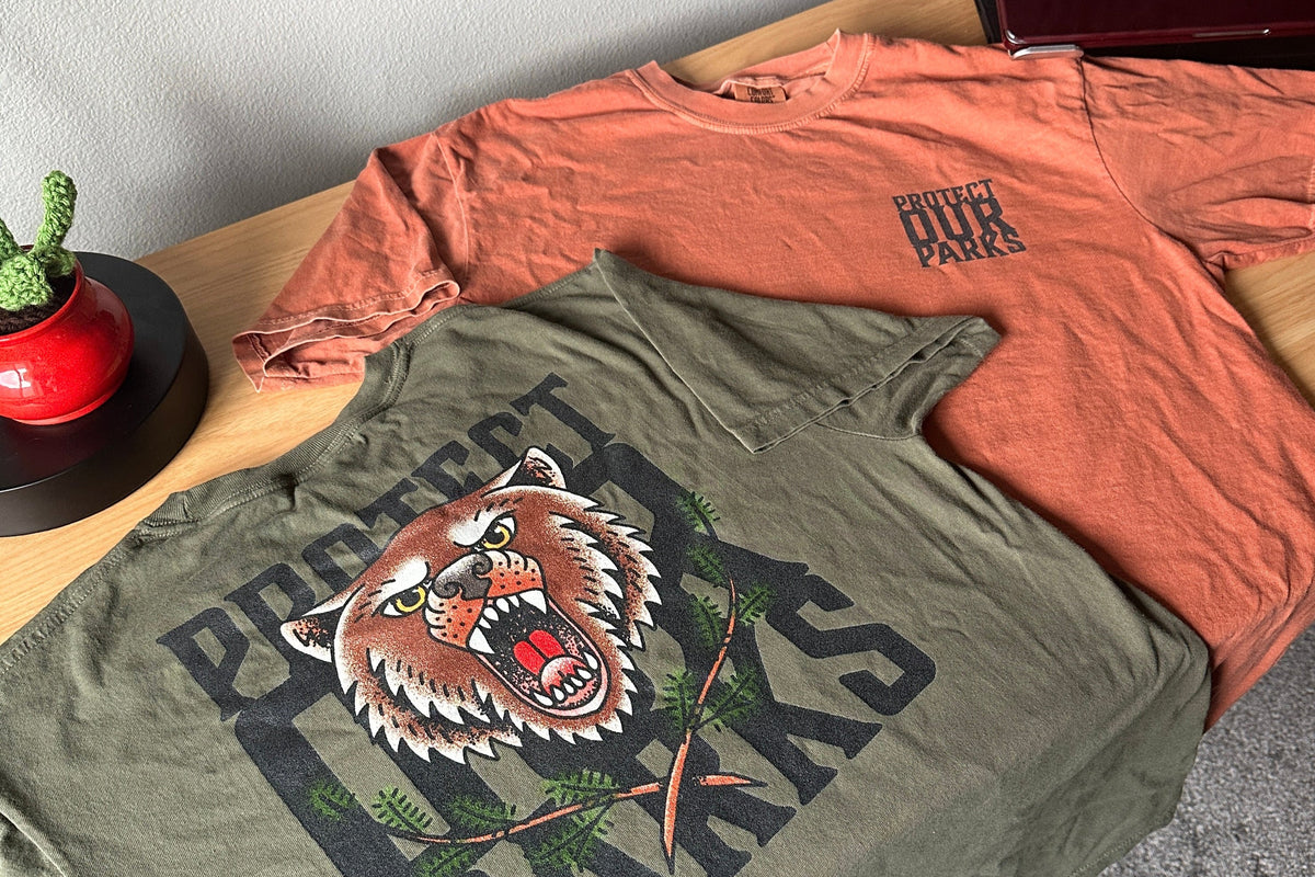 Green and orange t-shirts with a bear graphic and text on a wooden surface