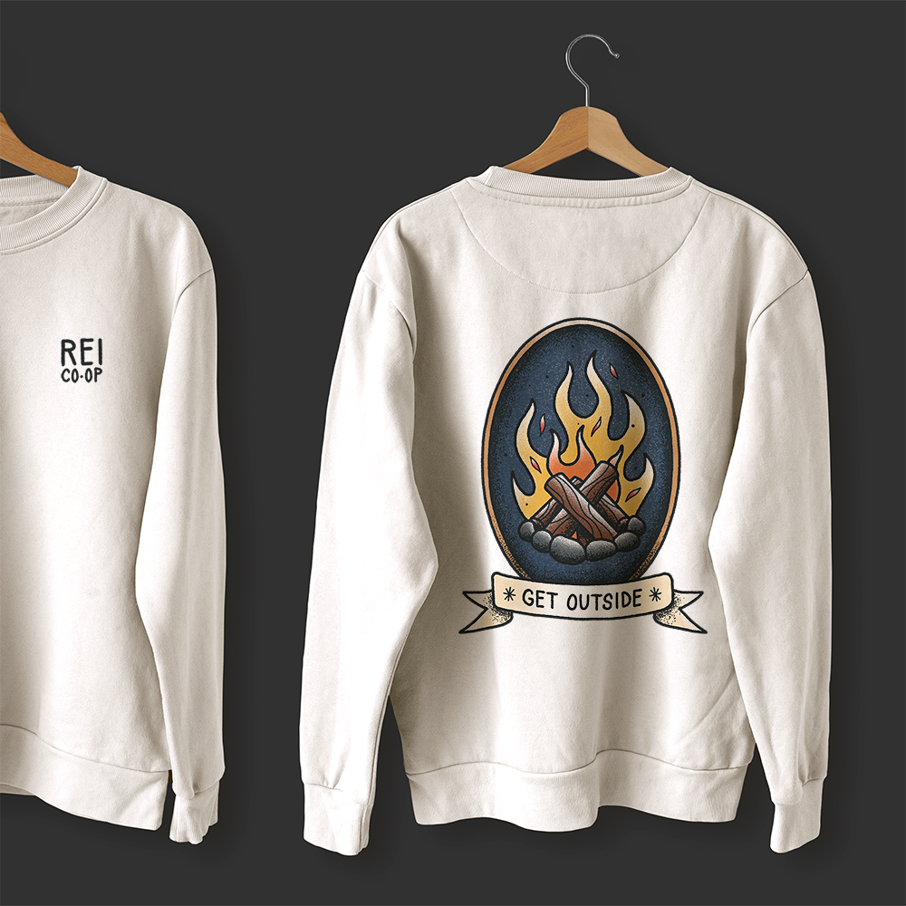 A white sweatshirt with an illustration of a campfire, on a hanger in front of a dark background.