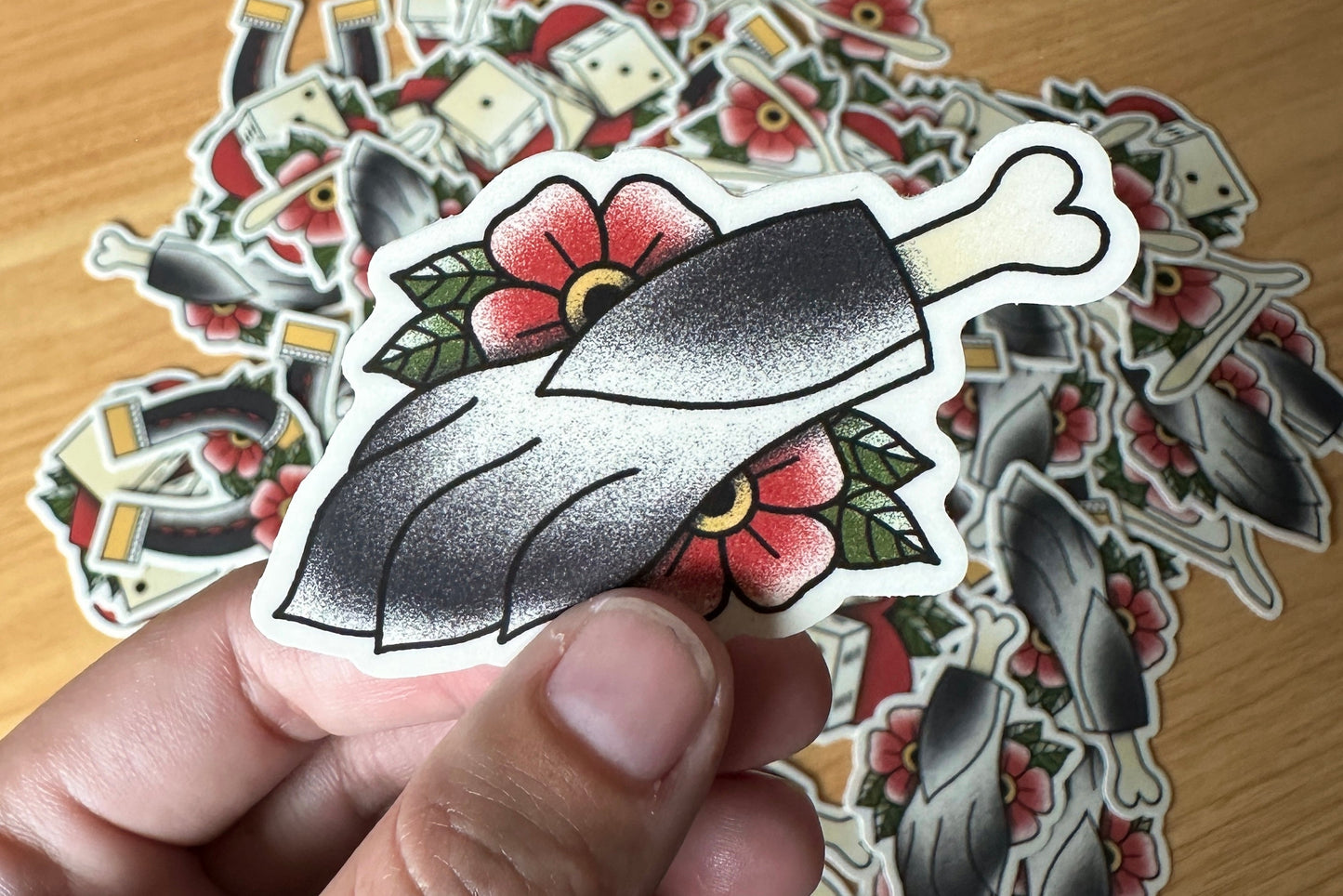 Hand holding a tattoo-style rabbit's food sticker with more stickers in the background on a wooden surface.