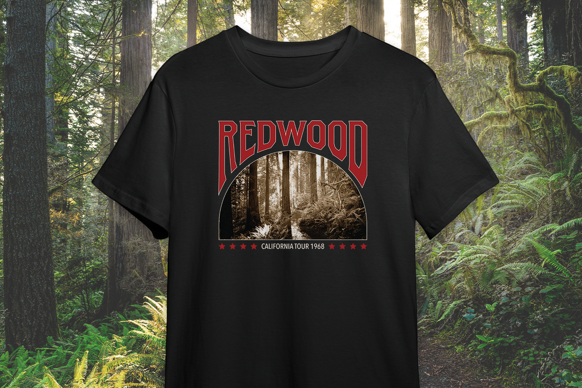 A black t-shirt with a 'Redwoods' graphic design, in front of a scenic background