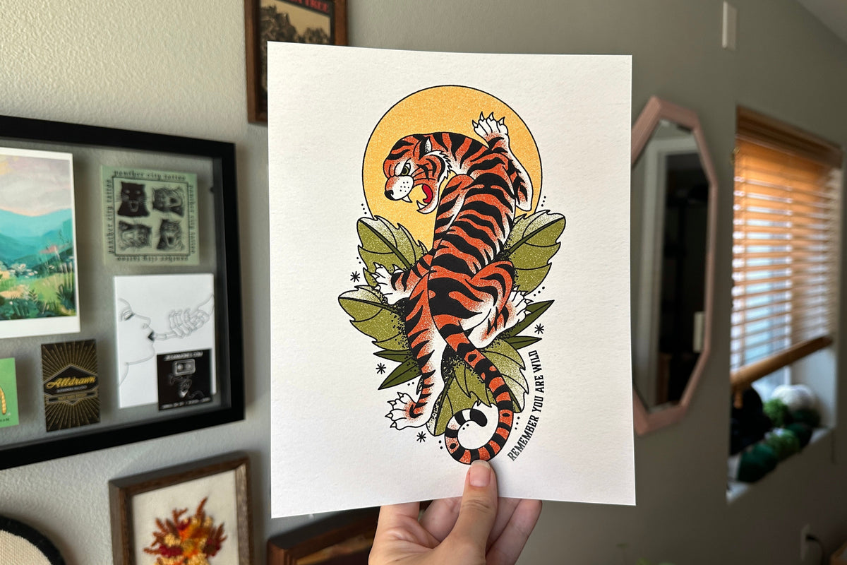 Person holding a print of a tiger design in a room with framed pictures on the wall.