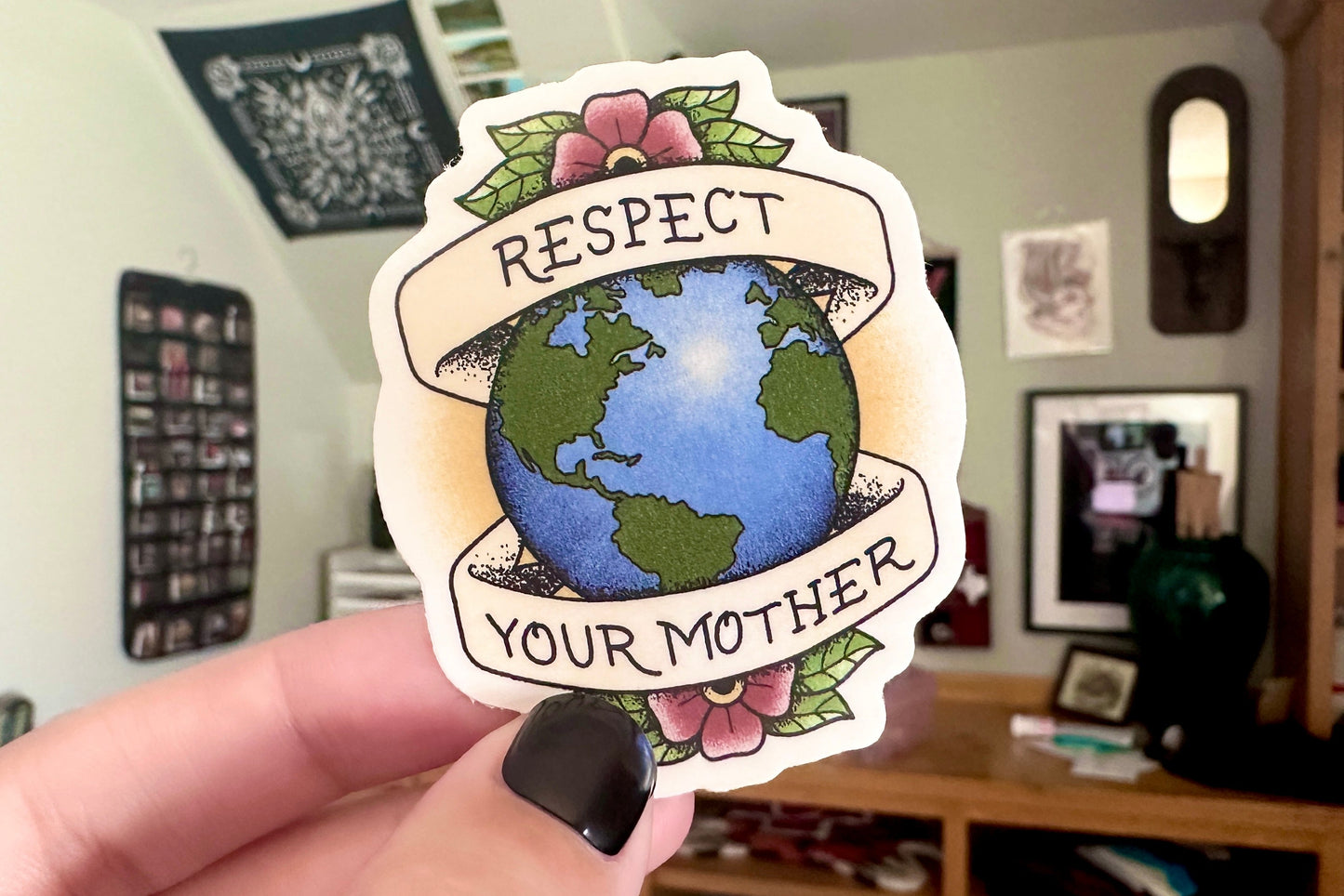 Sticker with 'Respect Your Mother' text held in a hand, with a blurred indoor background.