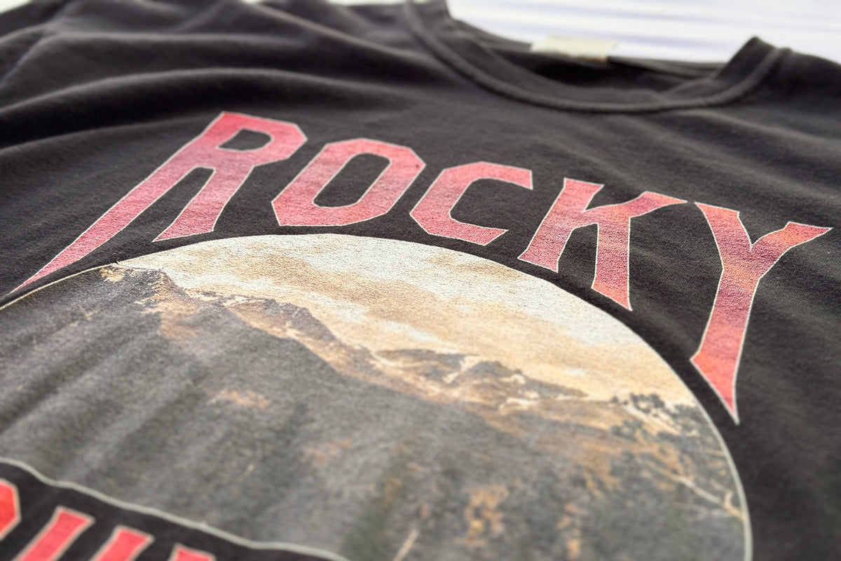 Black t-shirt with 'Rocky' text and mountain graphic, close-up view.