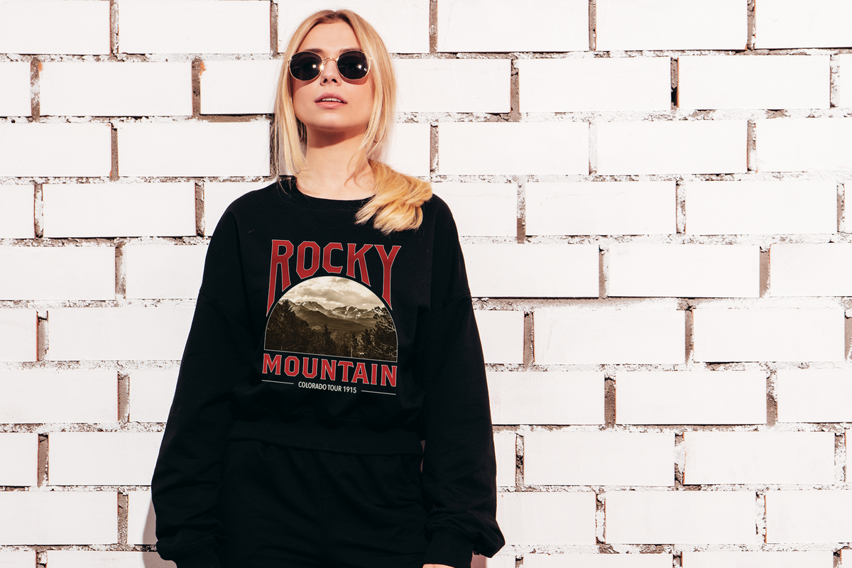 Person wearing a black sweatshirt with 'Rocky Mountain' design against a white brick wall.