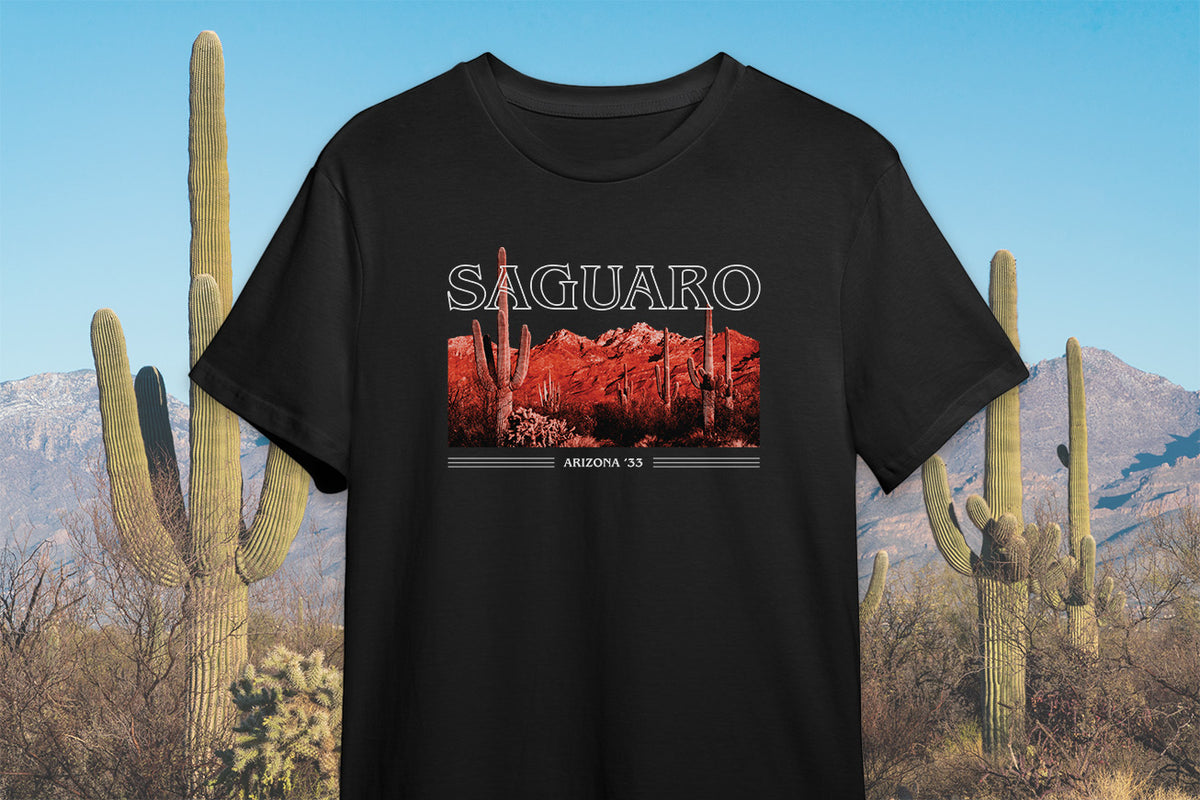 Black t-shirt with 'SAGUARO' text and a graphic of a cactus in red tones, set against a desert backdrop with cacti.
