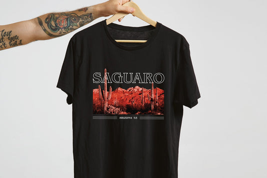 A black t-shirt with a 'Saguaro' graphic design, on a hanger in front of a white background