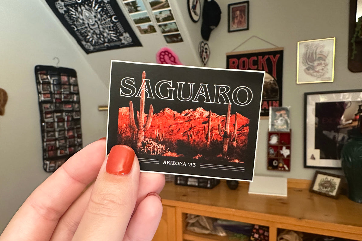 Hand holding a 'Saguaro' sticker against a room background.