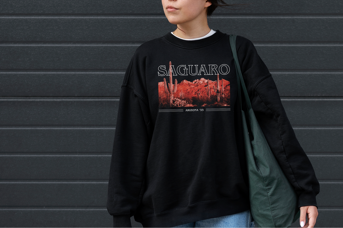 Person wearing a black sweatshirt with 'Saguaro' design against a gray wall
