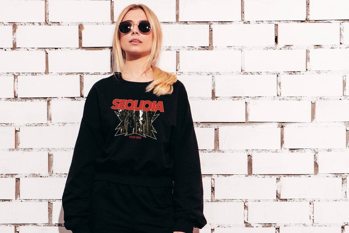 Person wearing a black sweatshirt with red and white 'Sequoia' design against a textured white brick wall.