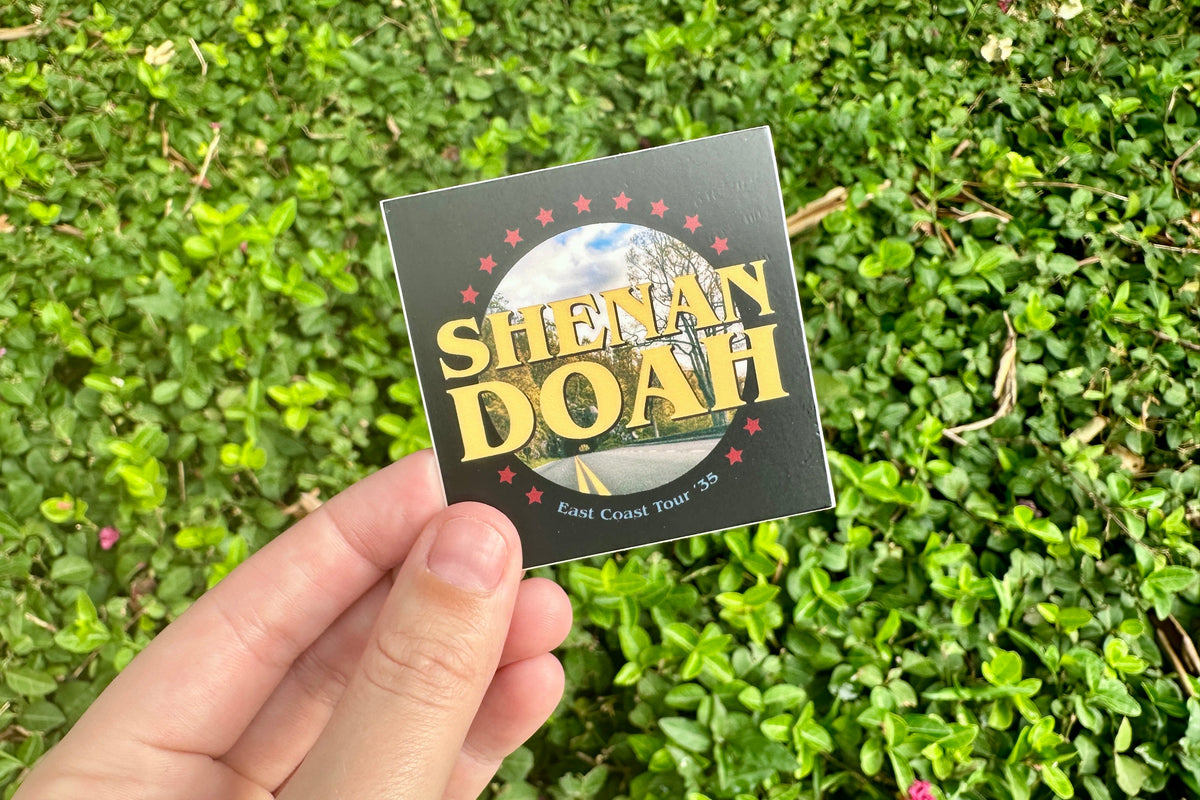 Hand holding a 'Shenandoah' sticker with a green grass background