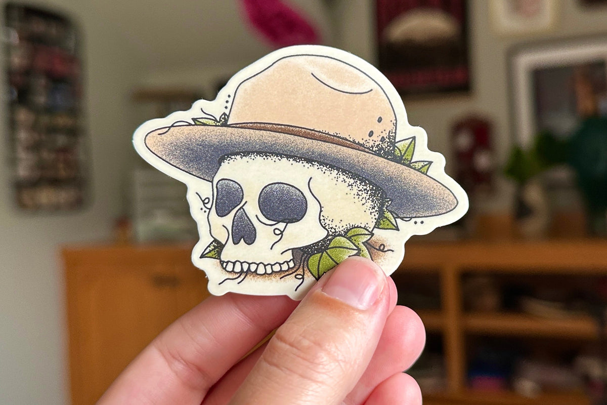 Skull with a hat sticker held in front of a blurred indoor background