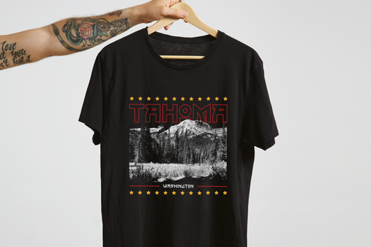 Black t-shirt with a graphic design of a mountain and text on a hanger, in front of a white background