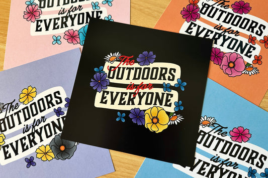 Colorful posters with 'The Outdoors is for Everyone' text and floral designs on a wooden surface.