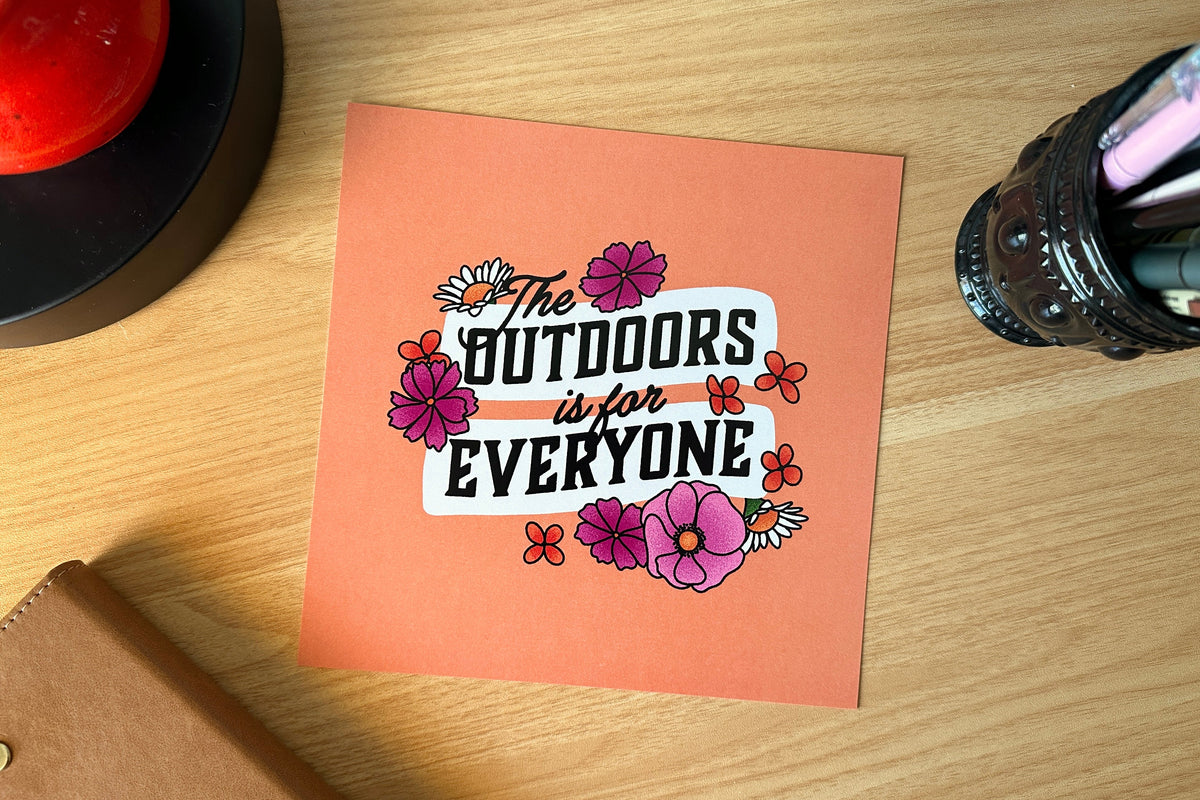 Art print with 'The Outdoors is for Everyone' text on a wooden surface