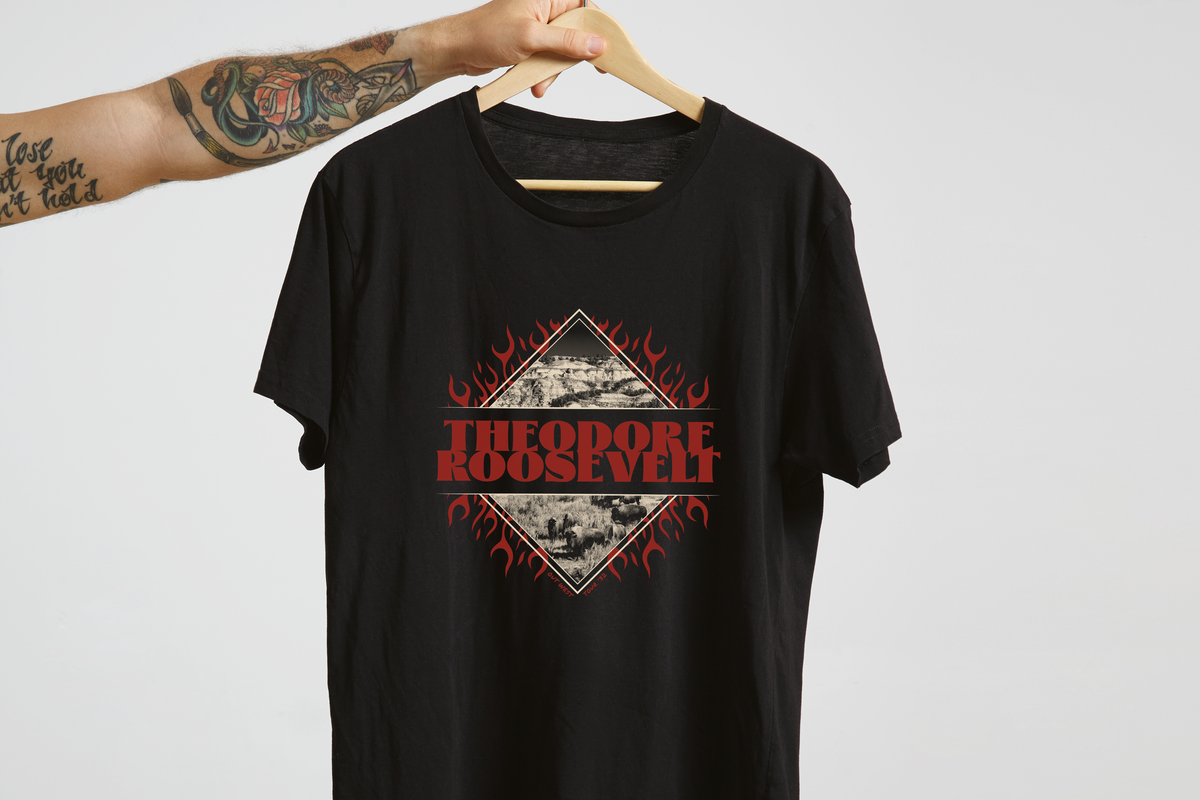 Black t-shirt with 'Theodore Roosevelt' graphic design on a hanger against a light gray background