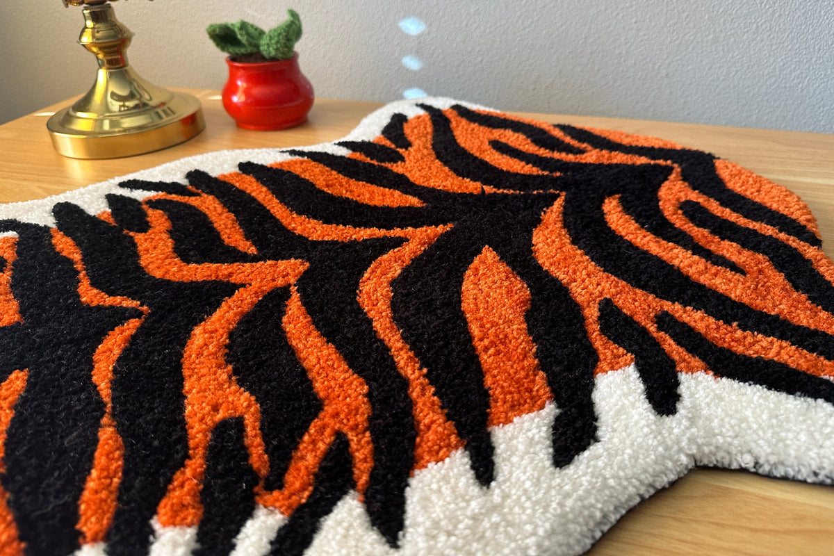 Tiger stripe patterned rug on a wooden surface with a small plant and decorative item in the background.