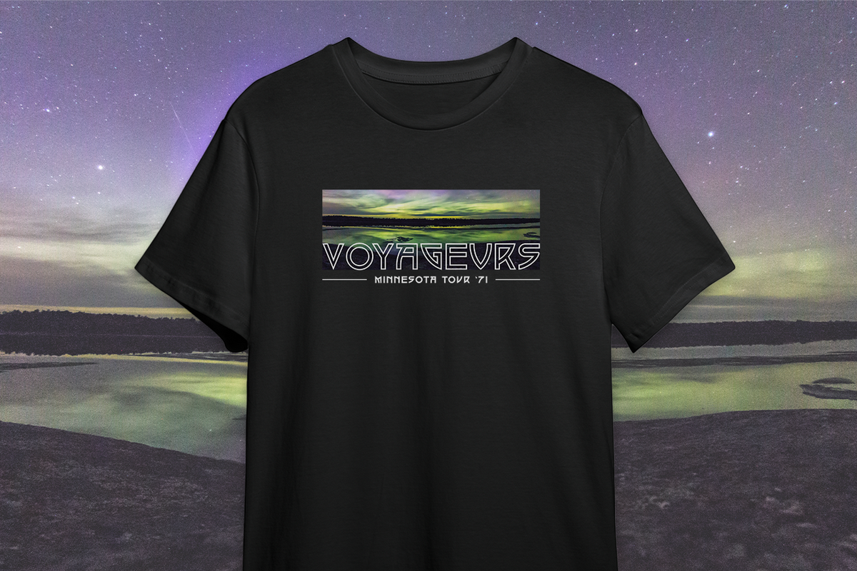 A black t-shirt with a printed design featuring the name 'VOYAGEURS' and an image of a nightscape with stars and a body of water in the background.