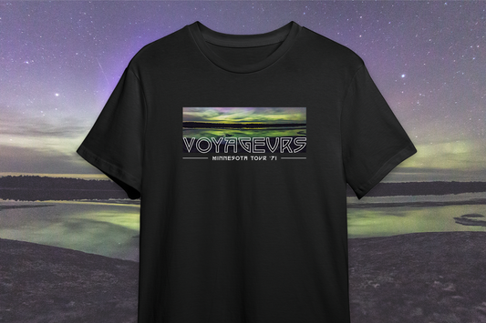 A black t-shirt with a printed design featuring the name 'VOYAGEURS' and an image of a nightscape with stars and a body of water in the background.