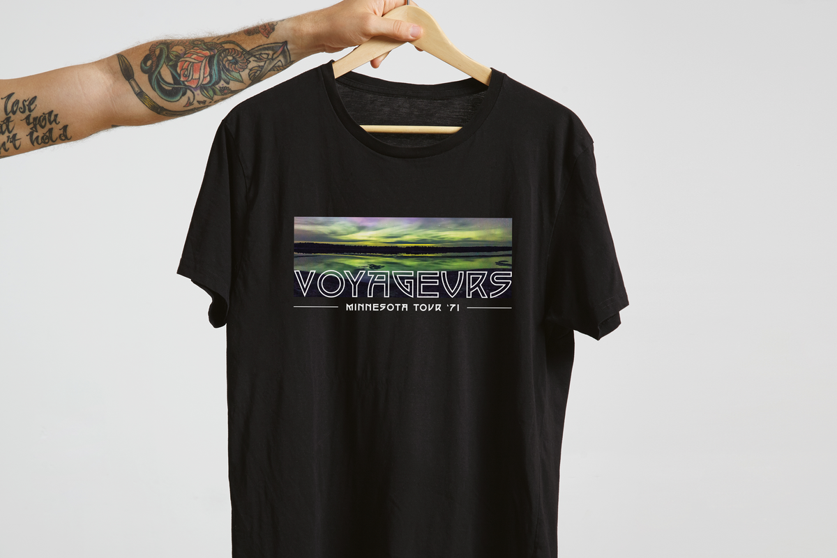 Black t-shirt with 'Voyageurs' graphic design on a hanger against a light gray background