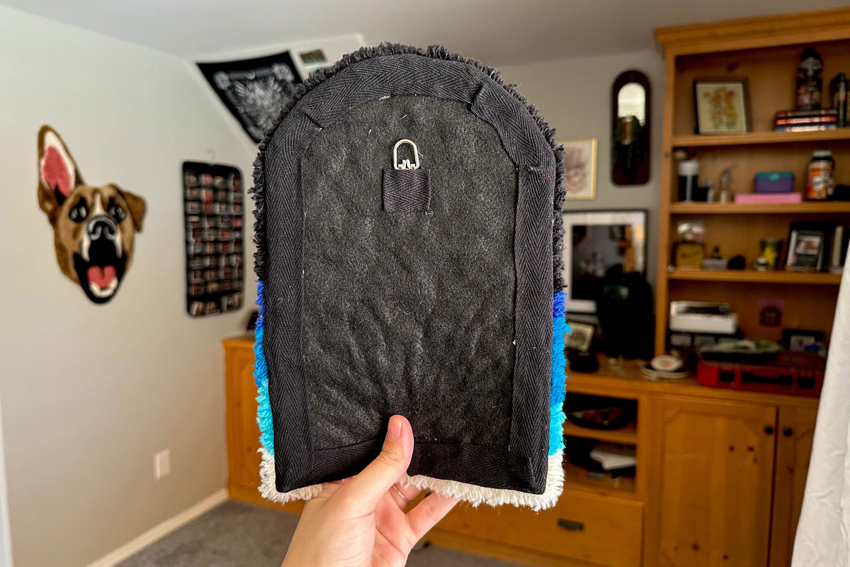 A person holding up the back of a tufted wall hanging in a room.