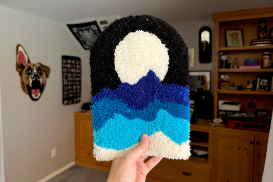 A person holding up a blue and black tufted wall hanging in an indoor setting
