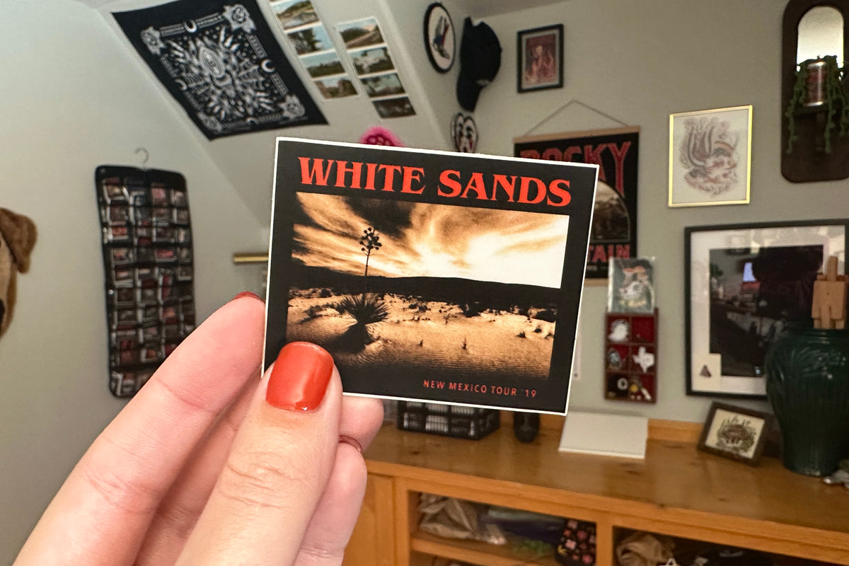 Hand holding a 'White Sands' sticker in a room with various decorations.