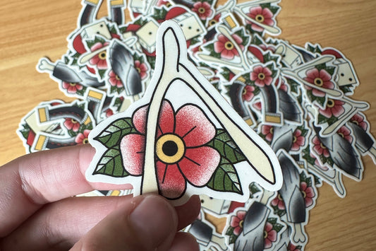Hand holding a wishbone sticker on a wooden surface with more stickers.