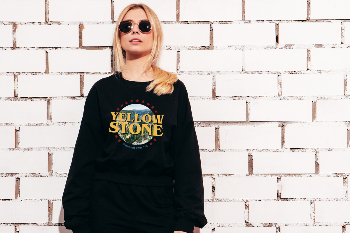 Person wearing a black sweatshirt with 'Yellowstone' design against a white brick wall