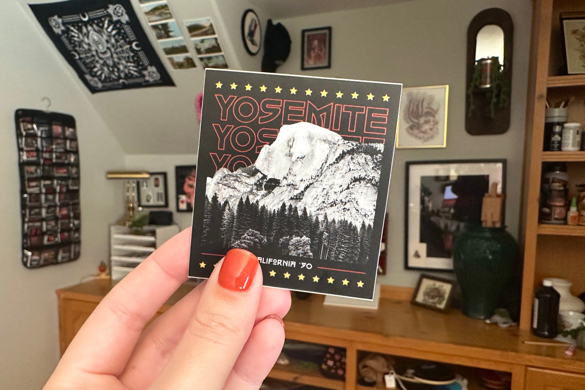 Hand holding a Yosemite National Park sticker in a room with decor and furniture.
